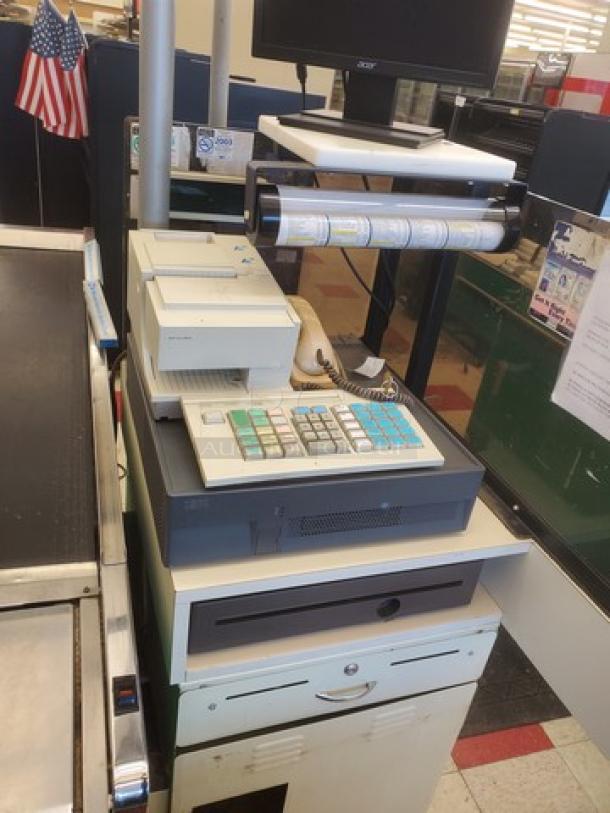 Supermarket checkout counter with register, receipt printer, and scanner. Includes cash drawer and conveyor belt. Good condition.