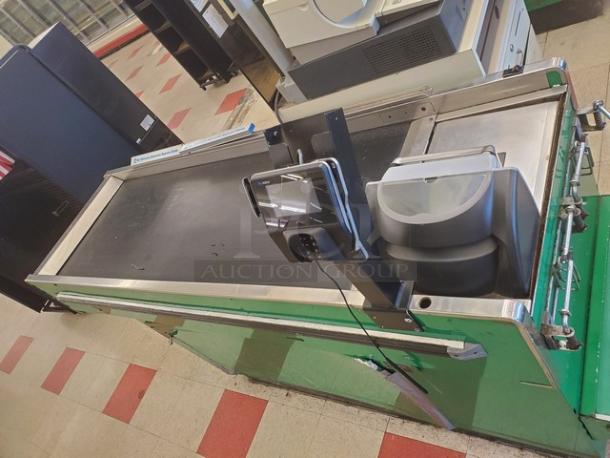 Supermarket checkout counter with conveyor belt, card reader, and bagging area. Green base, used condition, durable design.