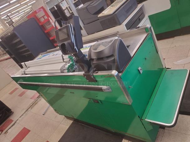 Supermarket checkout counter with green panels, conveyor belt, and integrated payment terminal. Moderate wear.