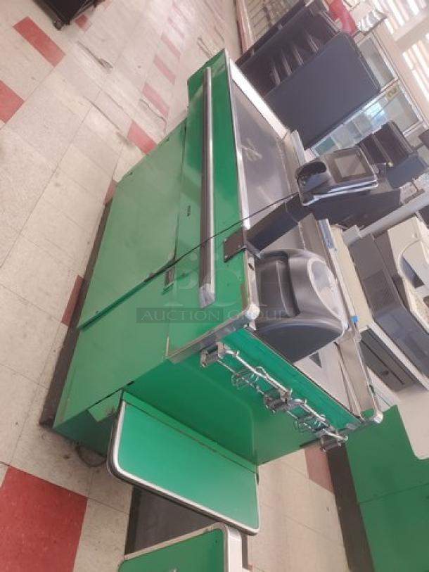 Supermarket checkout counter, green with metal accents, integrated scanner, conveyor belt, and cash drawer in used condition.