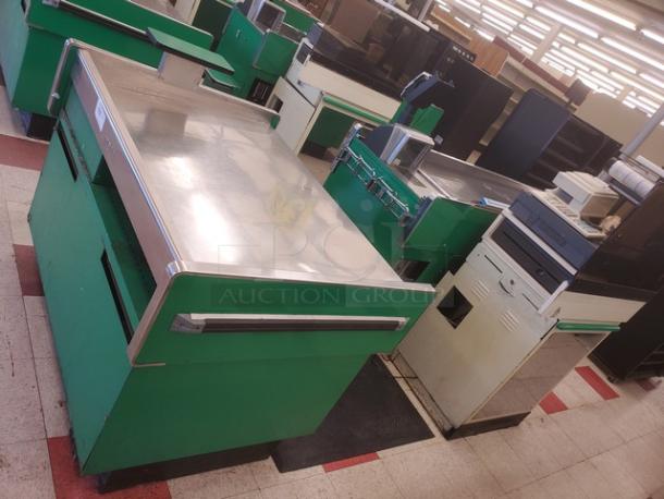 Vintage supermarket checkout counter with stainless steel top and green side panels. Includes conveyor belt and scanner. Fair condition.