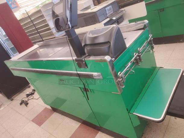 Green supermarket checkout counter with conveyor belt, scanner, bagging area, and sturdy metal frame. Some wear visible.