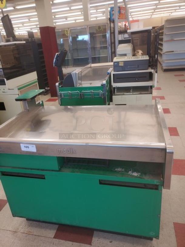 Supermarket checkout counter with green base, stainless steel surface, conveyor belt, scanner, and cash register; marked "Medix."