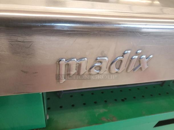 Madix supermarket checkout counter, stainless steel, visible wear, green under-shelf. Prominent "madix" logo on the front.