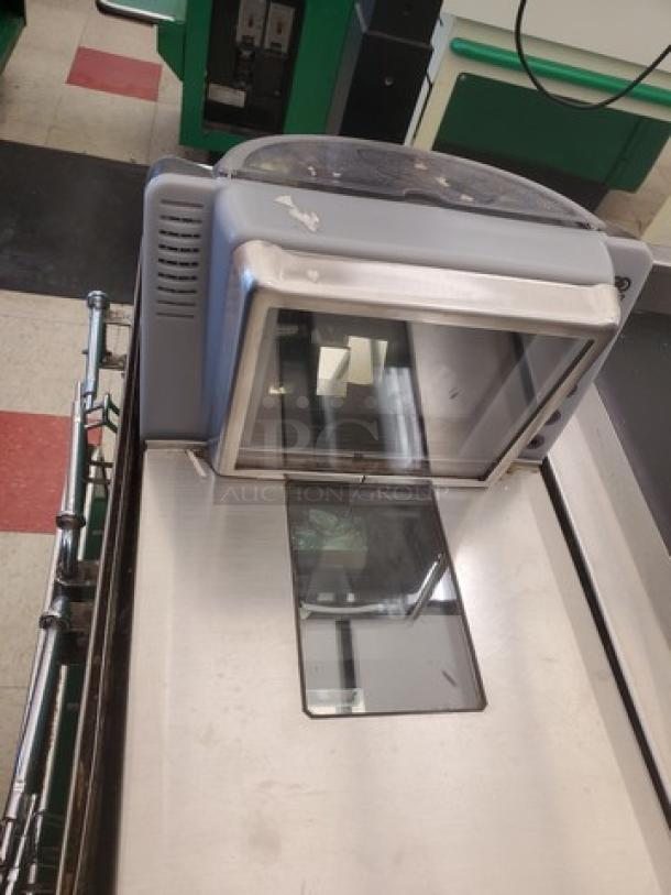 Supermarket checkout counter with stainless steel design, integrated barcode scanner, and bagging area. Good condition.