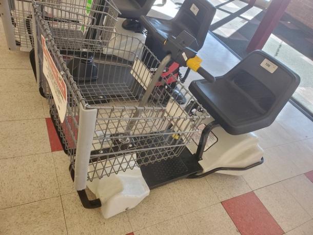 Motorized shopping cart with gray seat, basket, and handlebars. Used condition, ideal for mobility assistance.