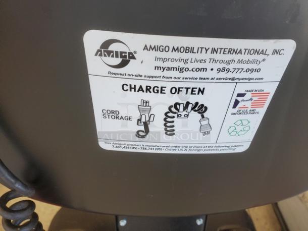 Motorized shopping cart with Amigo branding, labeled to charge often. Features cord storage. Made in USA.