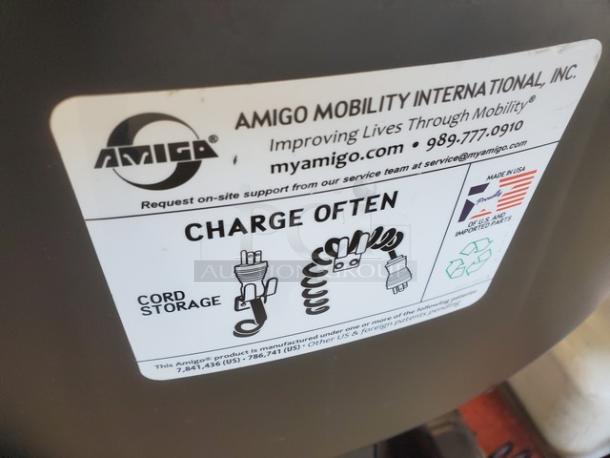Amigo Mobility motorized shopping cart with charge reminder label. Includes cord storage and USA manufacturing details.