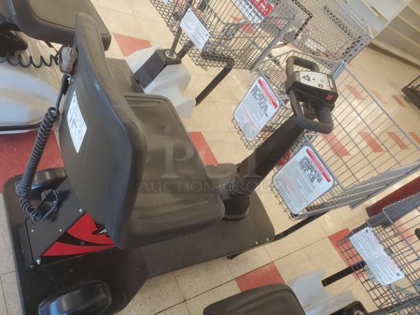 Motorized shopping cart with basket, black seat, and steering controls. Features warning labels, in a store setting, good condition.