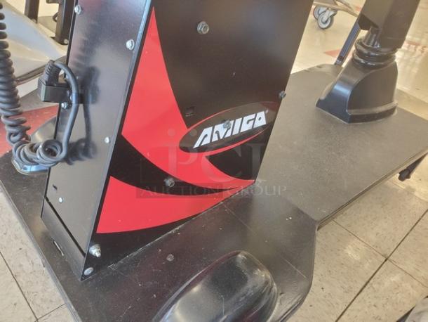 Motorized shopping cart with "Amigo" branding, featuring sturdy platform and control handle. Good condition.