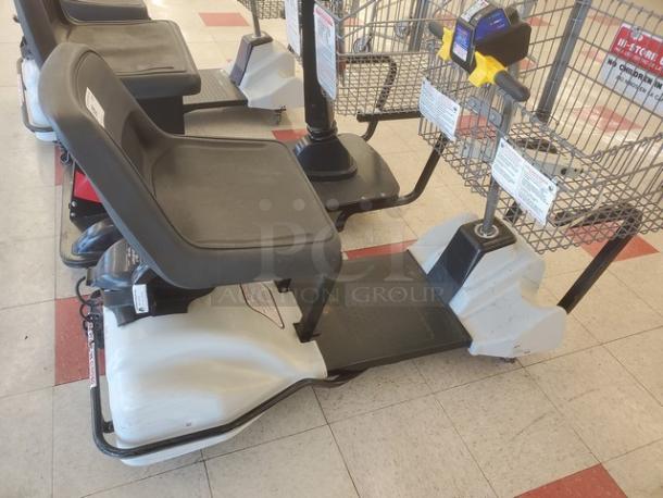 Motorized shopping cart, black seat, attached front basket, conditional wear visible, control panel with speed settings.