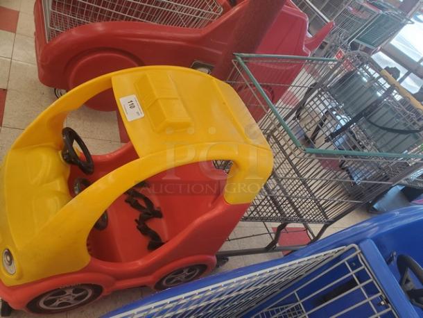 Yellow and red cartoon car shopping cart with steering wheel and child seat harness. Tag visible on top reads "114."