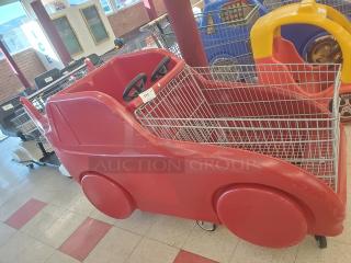 Red car-shaped shopping cart with steering wheels, metal basket, and molded plastic body. Ideal for child-friendly shopping.