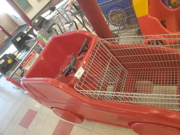 Red car-shaped shopping cart with steering wheel, wire basket, and child seating. Used condition, features sturdy plastic body.