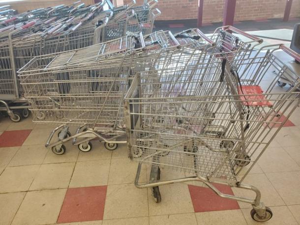 Lot of five used metal shopping carts with red handles, stored indoors. Visible wear on wheels and frames.