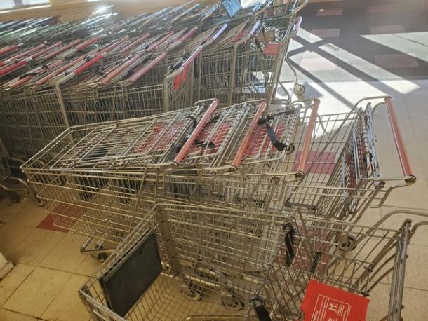 Lot of 5 metal shopping carts with red handles, in used condition. Some carts display red signs with store branding.
