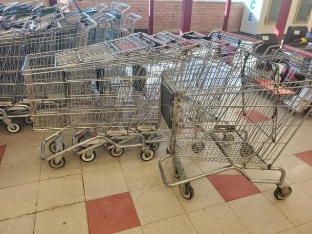 Lot of 5 metal shopping carts, used condition, stacked in a row, with sturdy wheels and child seats.