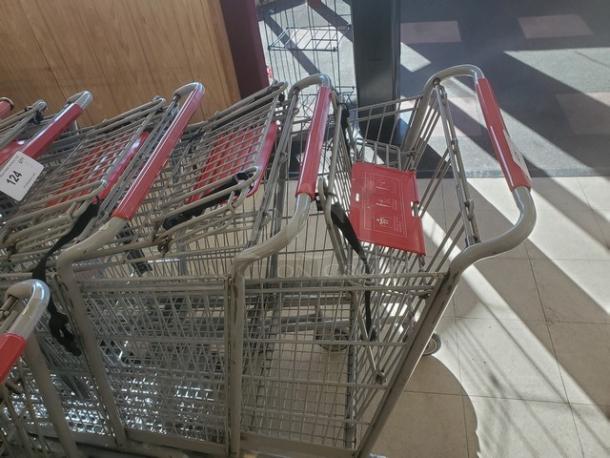 Lot of 3 metal shopping carts with red handles, in good condition, stacked indoors. Tags indicate "3XBID."