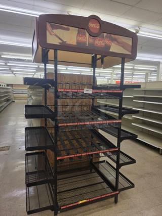 Gondola shelving unit with Coca-Cola branding, featuring multiple black metal shelves. Condition: used, buyer must remove.