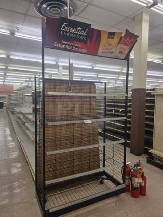 Retail display stand on casters with wire shelving. Features "Essential Everyday" branding. Suitable for store promotions.