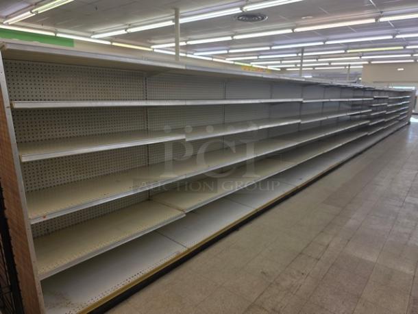 Double-sided gondola shelving, 65 feet long, white pegboard backing, multi-tiered, used condition, buyer must remove.