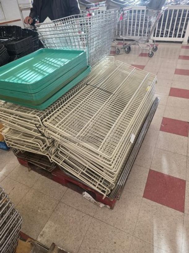 Four pallets of gondola shelving with wire racks and green trays, in used condition. Additional miscellaneous parts visible.