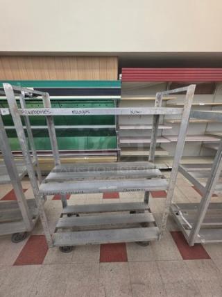Aluminum mobile shelf cart with three tiers, caster wheels, and labeled sections. Used condition with visible wear.