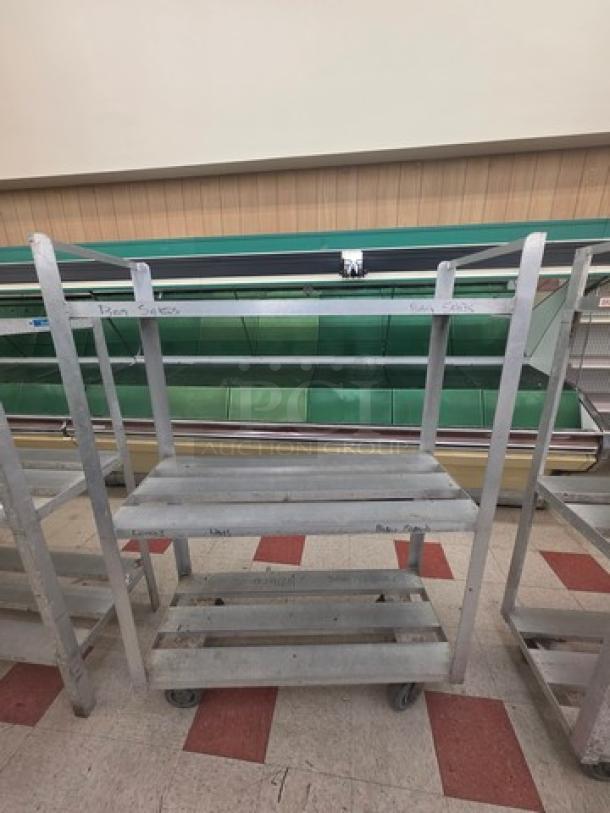 Aluminum mobile shelf cart with three tiers and caster wheels; sturdy design, lightly scuffed, ideal for storage and transport.