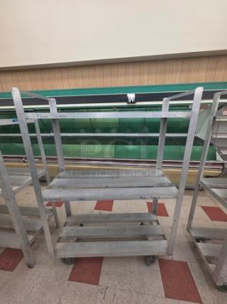 Aluminum mobile shelf cart with three tiers and caster wheels; sturdy design, lightly scuffed, ideal for storage and transport.