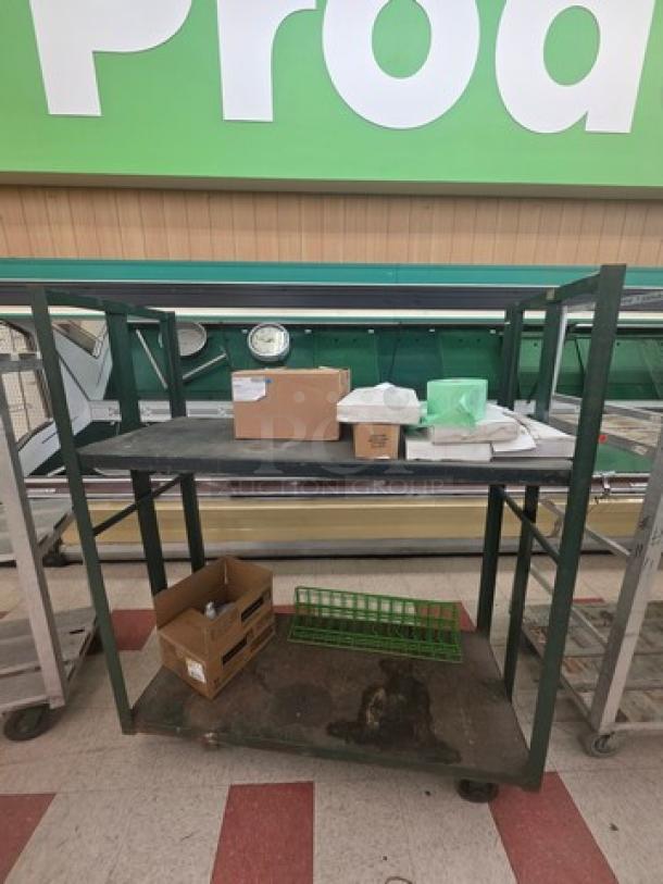 Industrial shelf cart with two metal shelves, green frame, used condition. Includes various stored items. Movable on wheels.