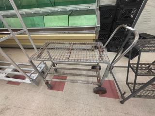Metal stocking cart with wire grid top, four wheels, and sturdy metal frame. Appears used, suitable for heavy-duty transport.