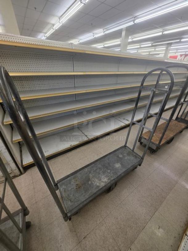 Heavy-duty stock cart with metal frame, flat base, and two vertical handles. Used condition, ideal for inventory transport.