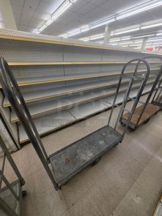 Heavy-duty stock cart with metal frame, flat base, and two vertical handles. Used condition, ideal for inventory transport.