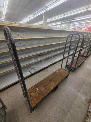 Metal stock cart with wooden base, visible wear, and two upright handles. Ideal for warehouse use. No labels visible.