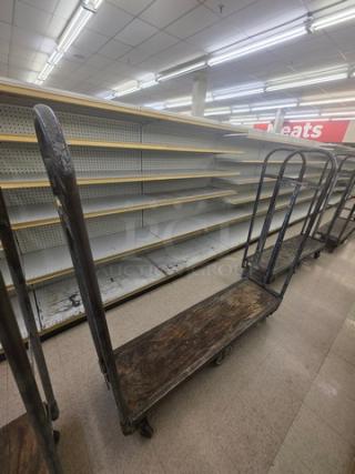 Weathered stock cart with wooden deck and metal handles, showing signs of use. Ideal for warehouse transport tasks.