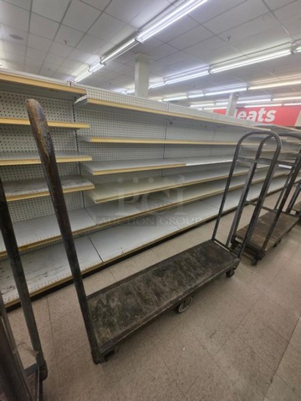 Heavy-duty stock cart with metal frame and platform, showing signs of wear. Ideal for moving merchandise in retail settings.