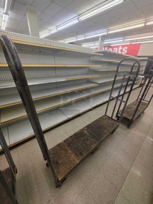 Industrial stock cart with metal frame and wood platform, displays wear. Ideal for transporting goods in a retail setting.