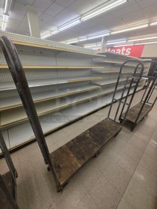 Industrial stock cart with metal frame and wood platform, displays wear. Ideal for transporting goods in a retail setting.