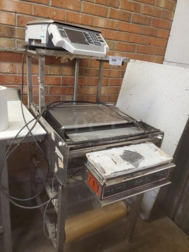 Commercial hand wrap station with digital scale, showing signs of wear. Features include sturdy metal construction and roll holder.