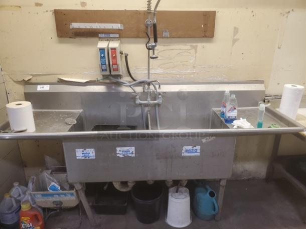 Stainless steel 3 compartment sink with faucet and sprayer. Labels indicate wash, rinse, and sanitize sections. Used condition.