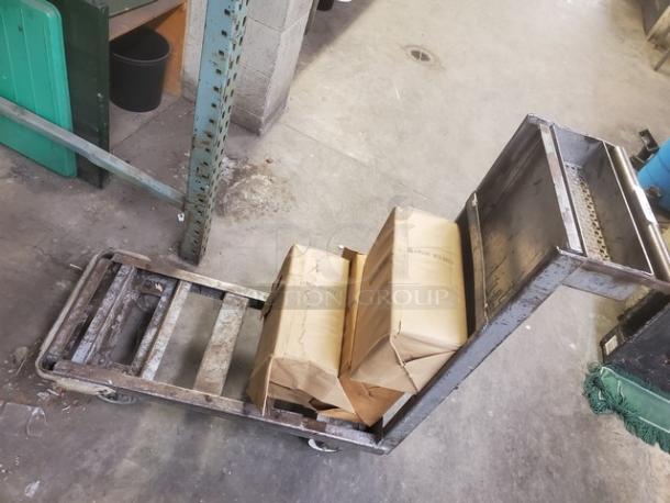 Metal retail dolly cart with dual wheels and handles. Some wear visible. Load includes two paper-wrapped items.