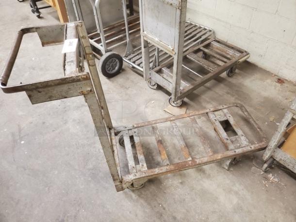 Rustic retail dolly cart, metal, worn condition, visible rust on frame, flat platform with handle, wheels intact.