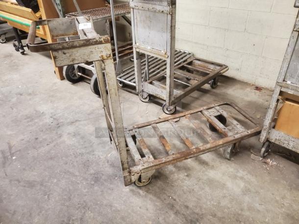 Rustic retail dolly cart with metal frame and four wheels. Visible wear indicates extensive use. Ideal for heavy-duty transport.
