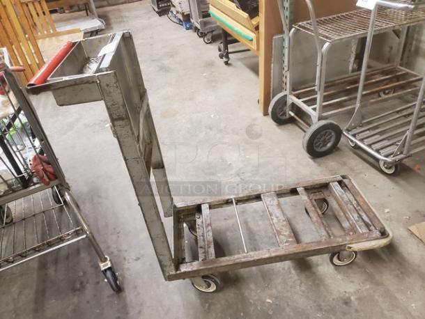 Metal retail dolly cart with a handle, four wheels, and a flat base. Used condition, visible wear and rust on frame.