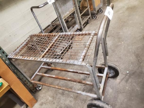 Industrial retail dolly cart with metal grid surface, showing signs of rust and wear, two wheels per side, sturdy handle.