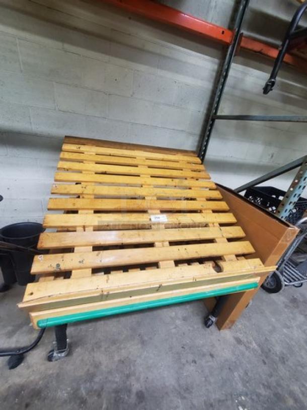 Wooden pallet roller, used condition, with sturdy slats and attached wheels for easy movement. Ideal for warehouse use.