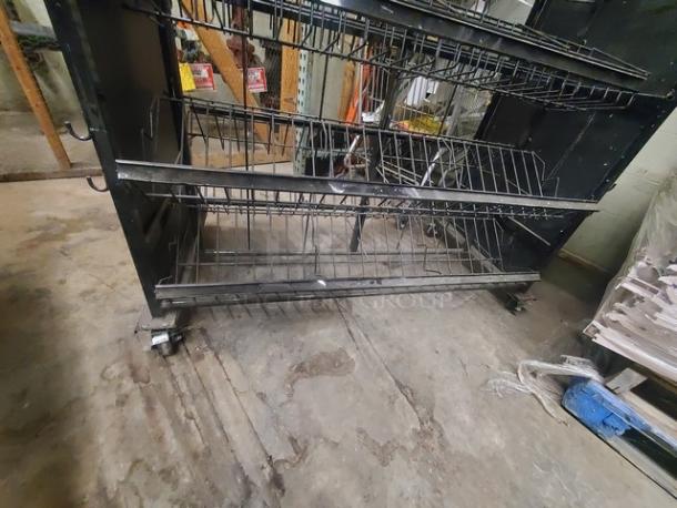 Metal wire display rack with three shelves, on wheels for mobility, in used condition. Suitable for retail display.