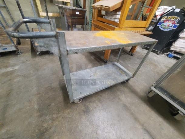 Heavy-duty metal utility cart with two shelves and casters. Visible wear and rust spots indicate used condition.