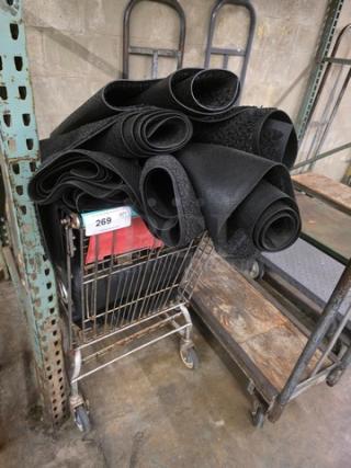 Shopping cart filled with rolled black rugs, item tag labeled "269," in warehouse setting.