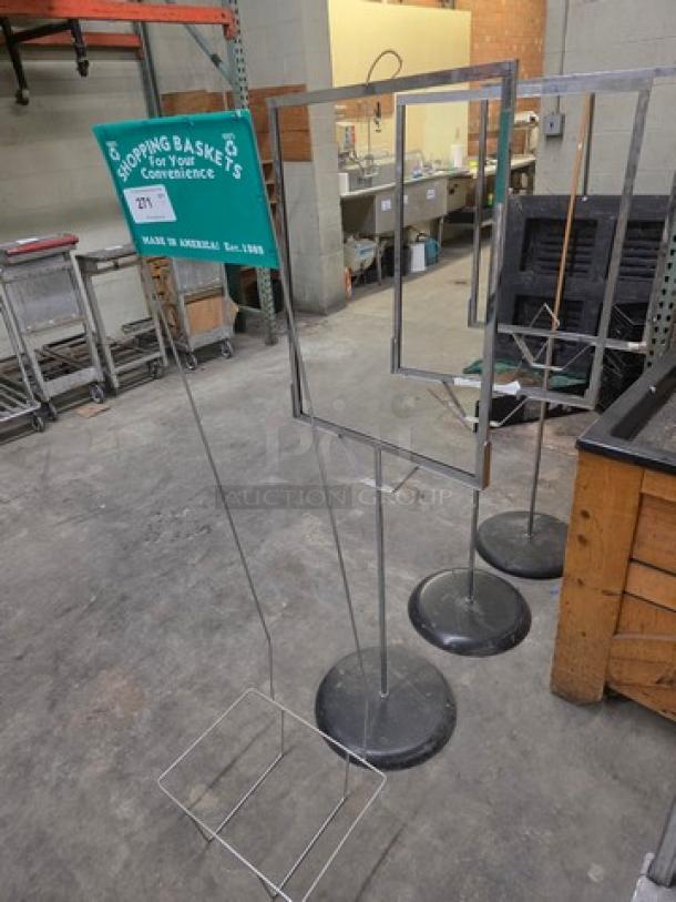 Lot of 4 floor-standing sign holders, metal frames with bases, good condition, one with "Shopping Baskets For Your Convenience" label.